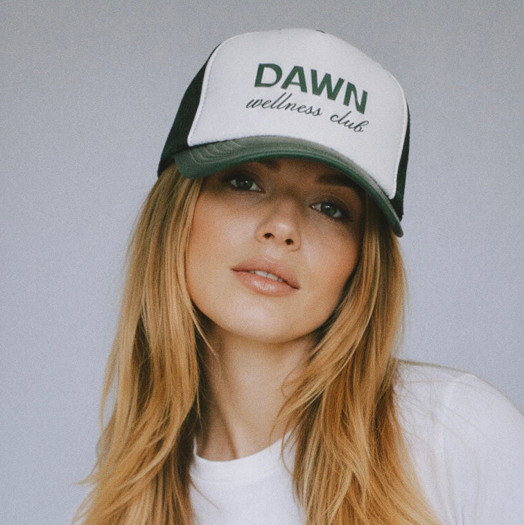 Woman wearing a cap with 'Dawn Wellness Club' text against a plain background
